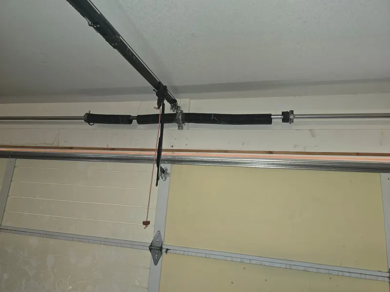 Broken torsion spring on the shaft above a garage door, with a gap in the coil where it snapped