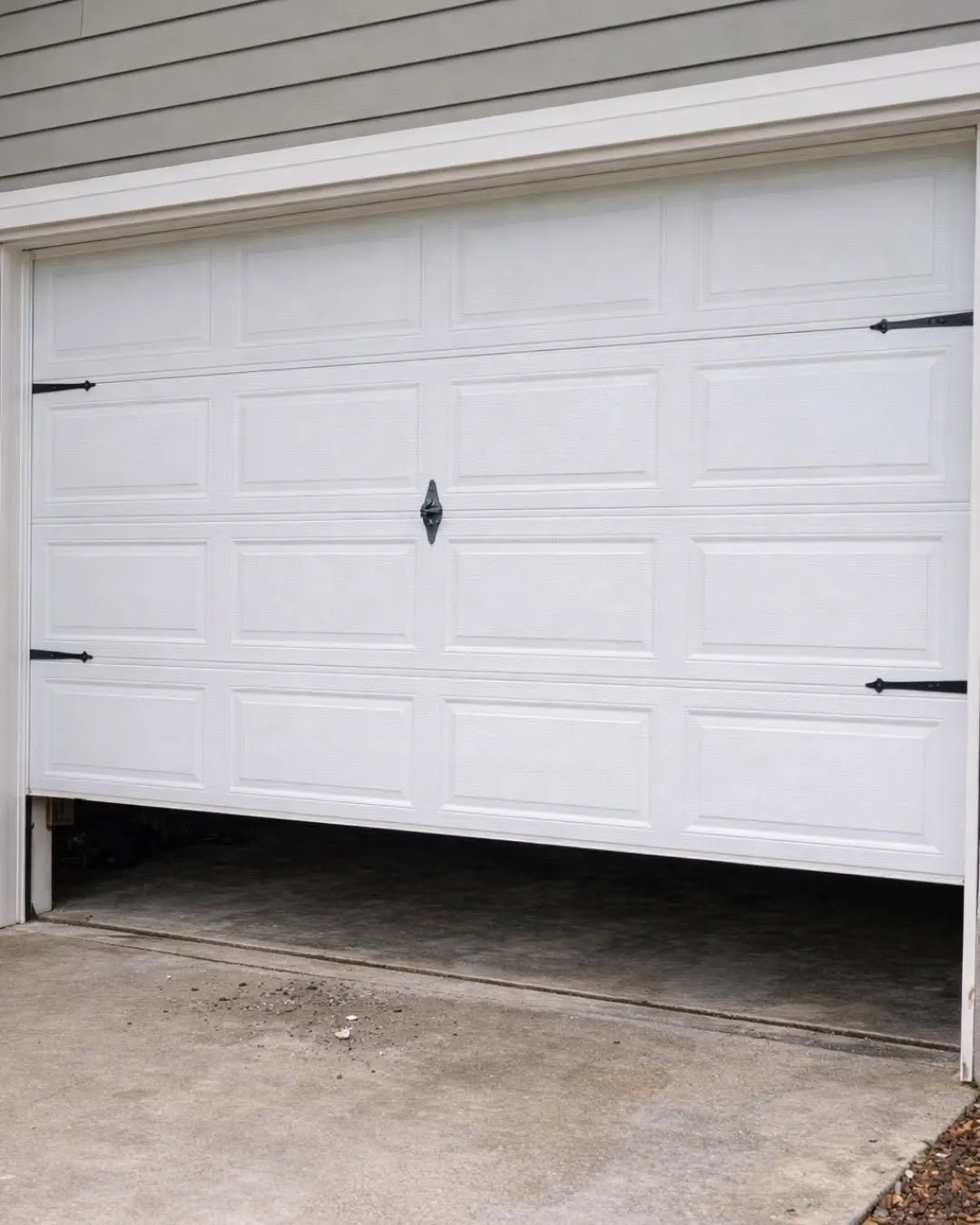White garage door stuck partly open and sitting crooked, higher on one side than the other