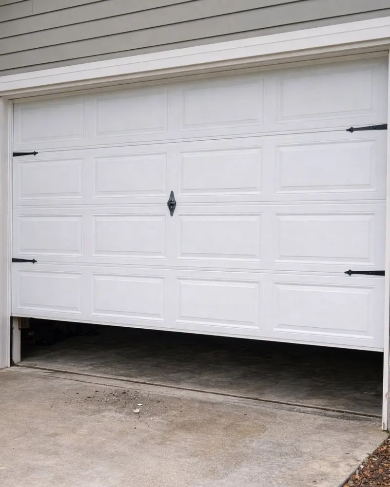 White garage door stuck partly open and sitting crooked, higher on one side than the other
