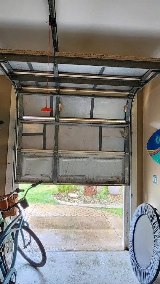 Garage door stopped partway open, seen from inside the garage with a bicycle beside it