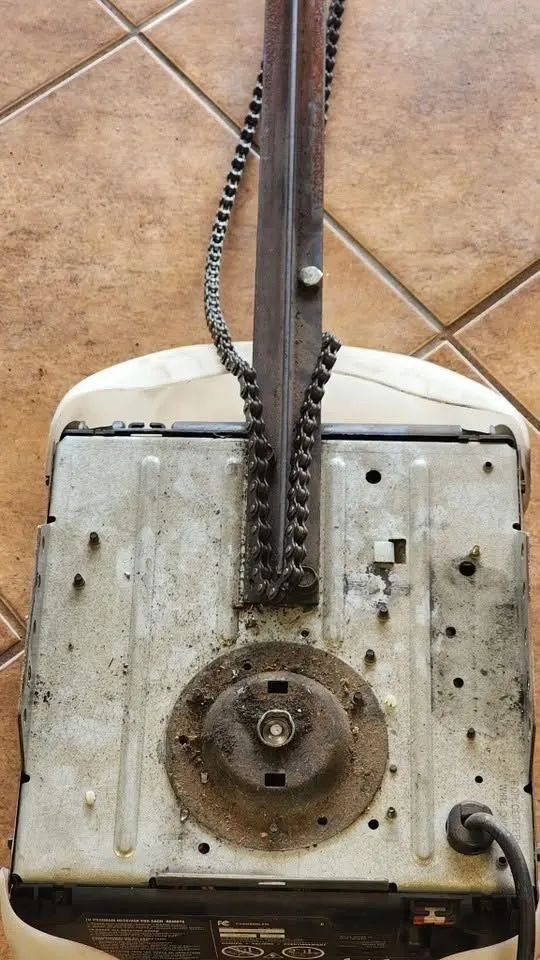 Underside of an old chain-drive garage door opener with a rusted, dirty drive sprocket